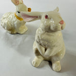 A pair of white vintage ceramic bunnies one with a yellow ribbon on its neck.