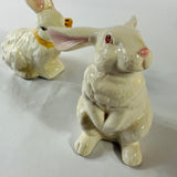 A pair of white vintage ceramic bunnies one with a yellow ribbon on its neck.