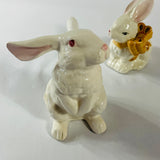 A pair of white vintage ceramic bunnies one with a yellow ribbon on its neck.
