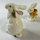 A pair of white vintage ceramic bunnies one with a yellow ribbon on its neck.