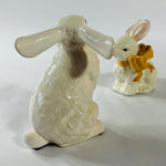 A pair of white vintage ceramic bunnies one with a yellow ribbon on its neck.
