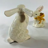 A pair of white vintage ceramic bunnies one with a yellow ribbon on its neck.