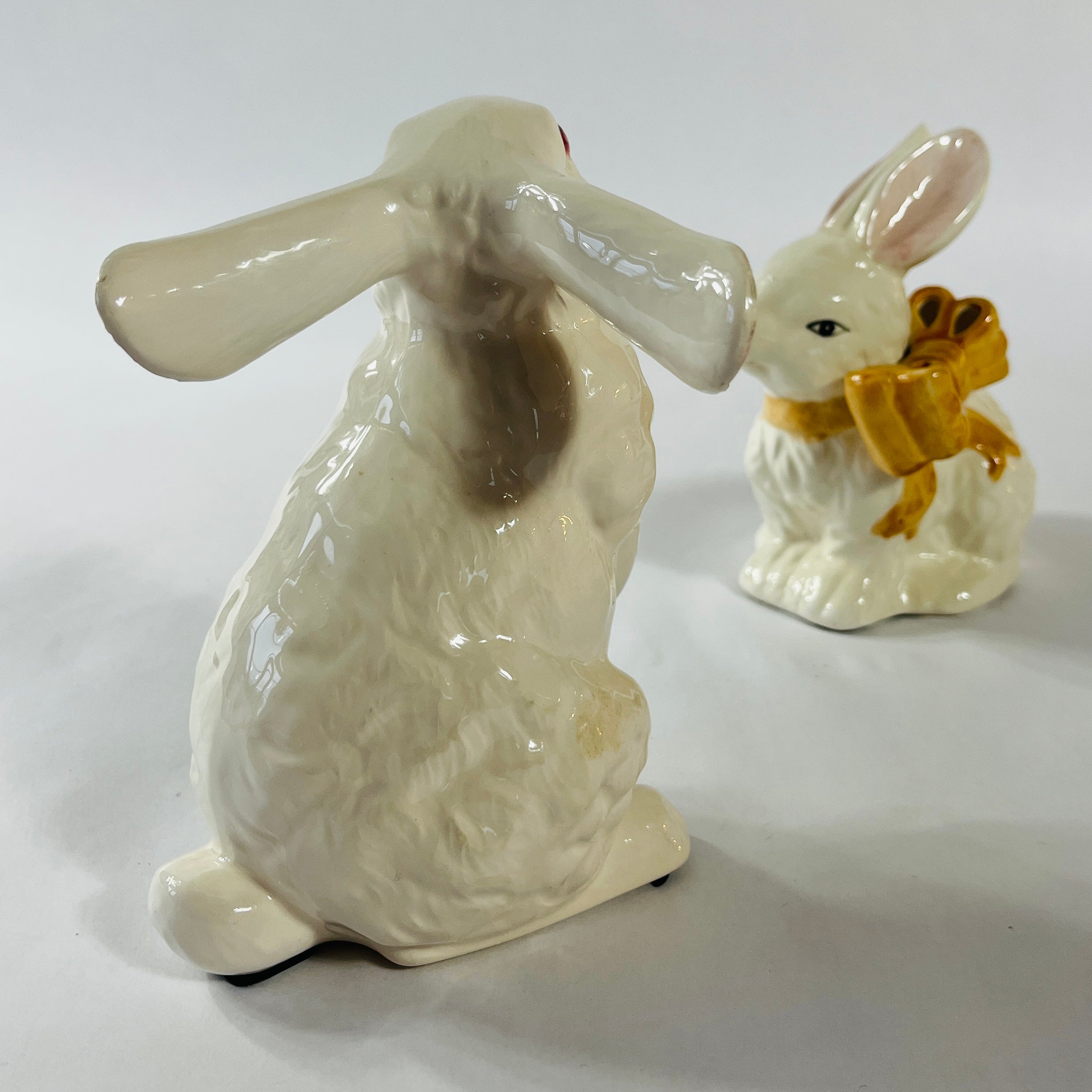 A pair of white vintage ceramic bunnies one with a yellow ribbon on its neck.