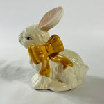 A pair of white vintage ceramic bunnies one with a yellow ribbon on its neck.