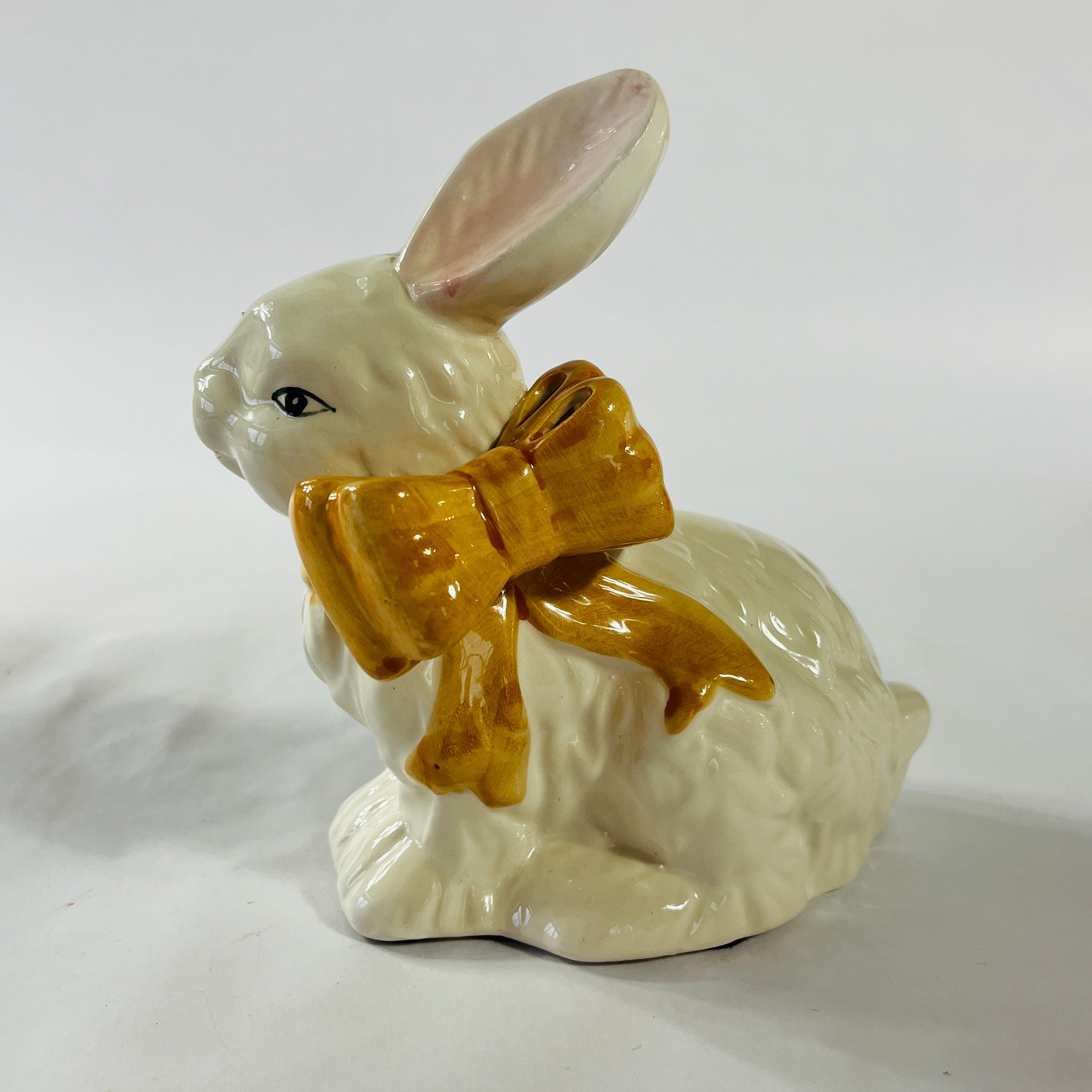 A pair of white vintage ceramic bunnies one with a yellow ribbon on its neck.