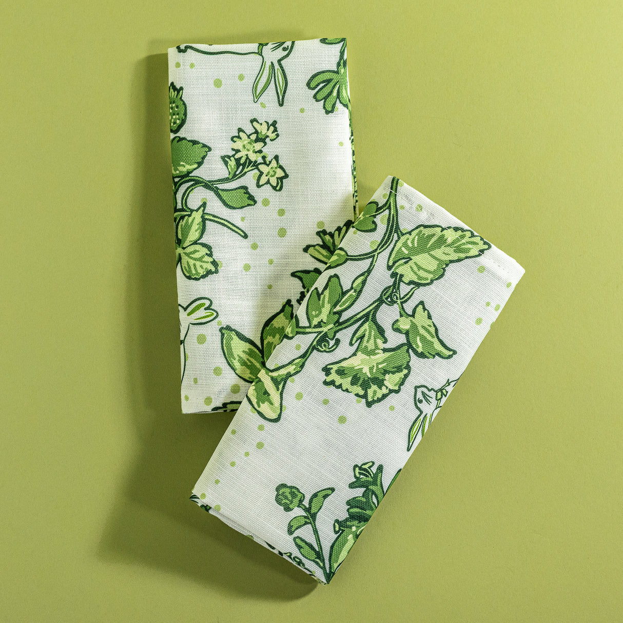 A pair of green bunny and strawberry print fabric Easter napkins against a green background.