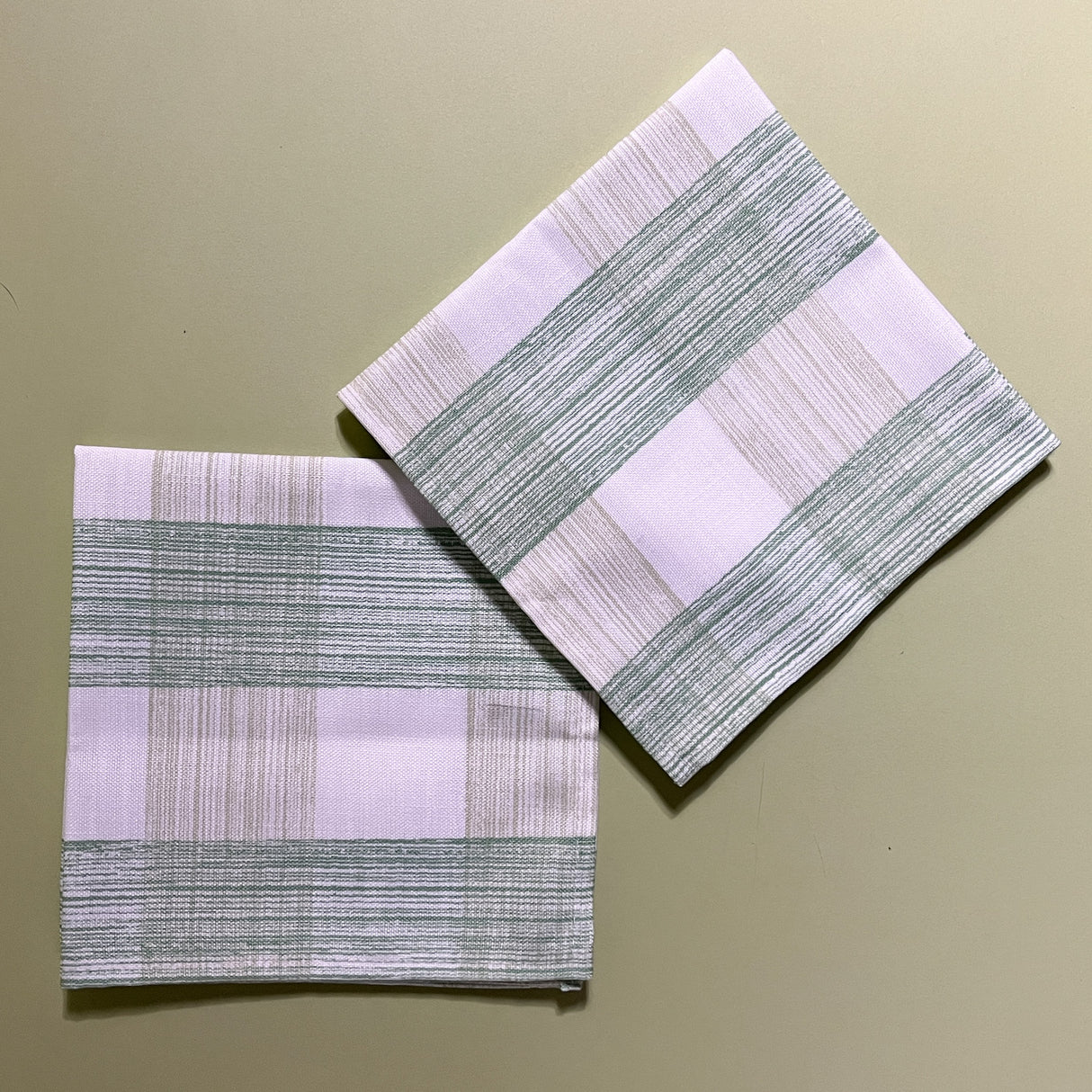 two green gingham dinner napkins in gin lane print fabric by madap cottage on a light green background