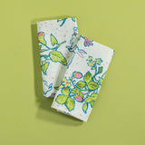 A pair of multicolor bunny and strawberry print fabric Easter napkins against a green background. 