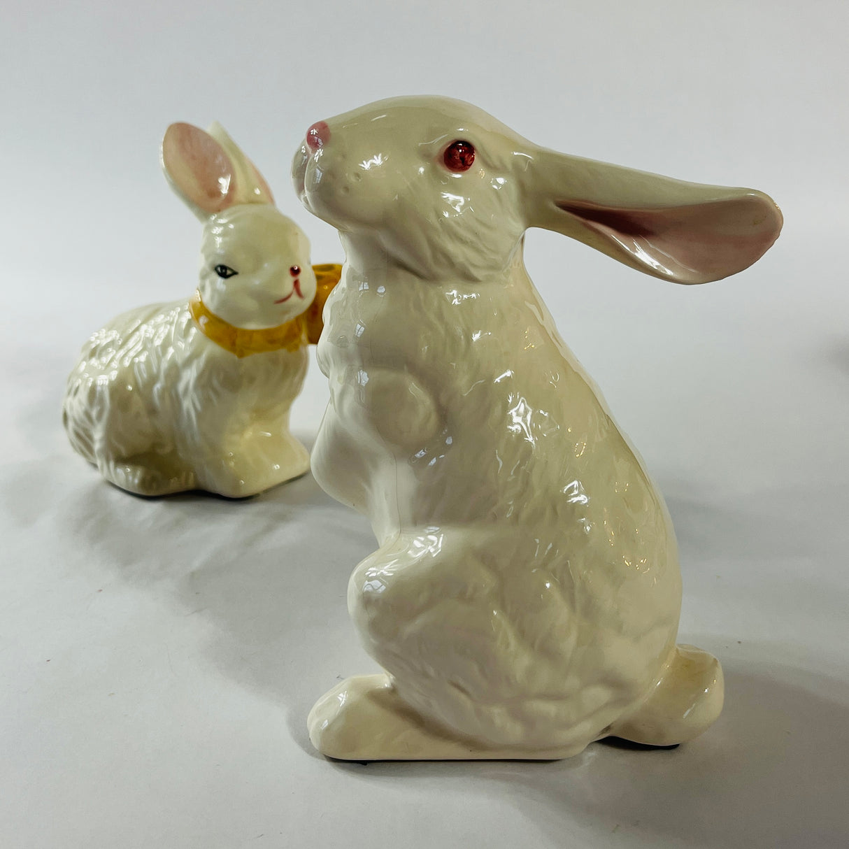 A pair of white vintage ceramic bunnies one with a yellow ribbon on its neck. 