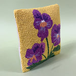 side view of a spring pillow with purple pansies on a yellow background.