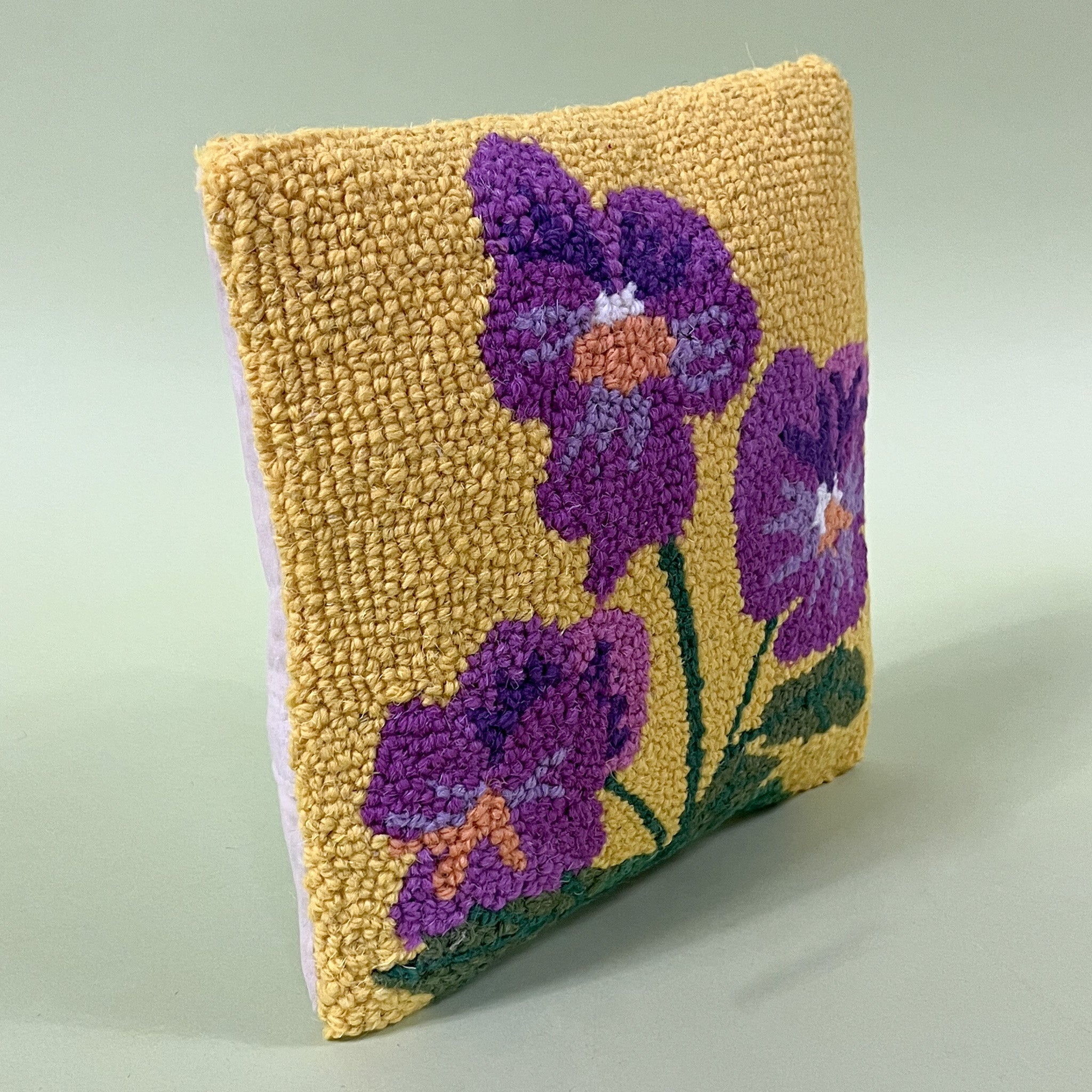side view of a spring pillow with purple pansies on a yellow background.