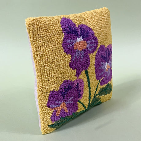 side view of a spring pillow with purple pansies on a yellow background. 