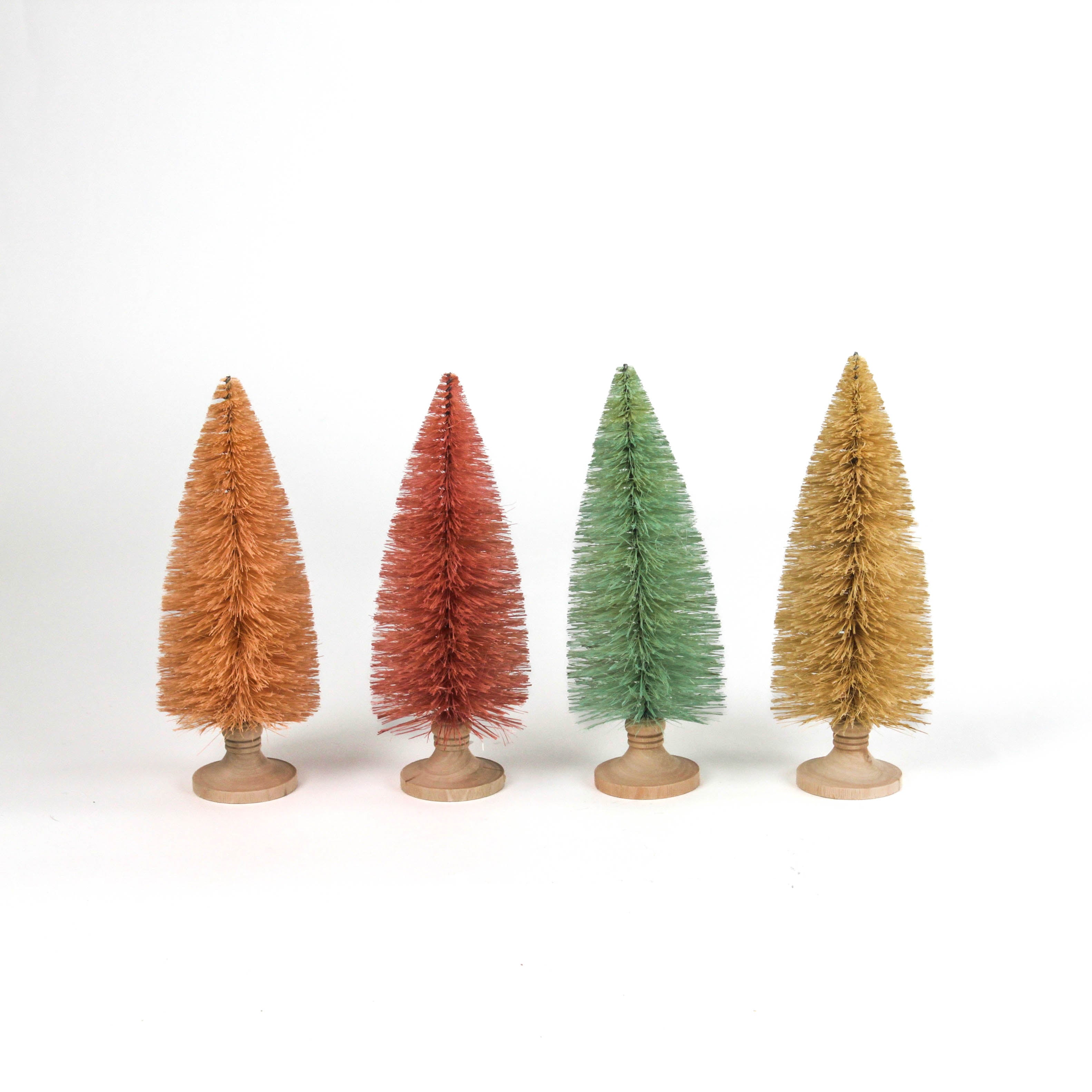 Four miniature bottle brush Christmas trees table decorations in light pink, pink, green and beige on a white background.