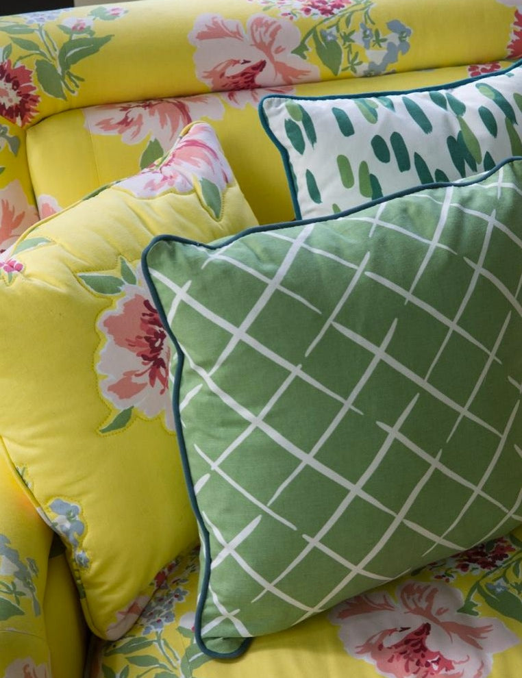 Decorative throw pillows with green lattice and botanical patterns styled on a bright yellow floral upholstered sofa.