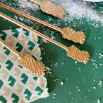 four gold pineapple drinks stirrers against a snowy green background. 