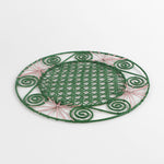 a pink and green round rattan placemat with green swirls and pink star woven motifs against a white backround.