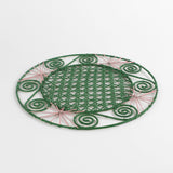 a pink and green round rattan placemat with green swirls and pink star woven motifs against a white backround.