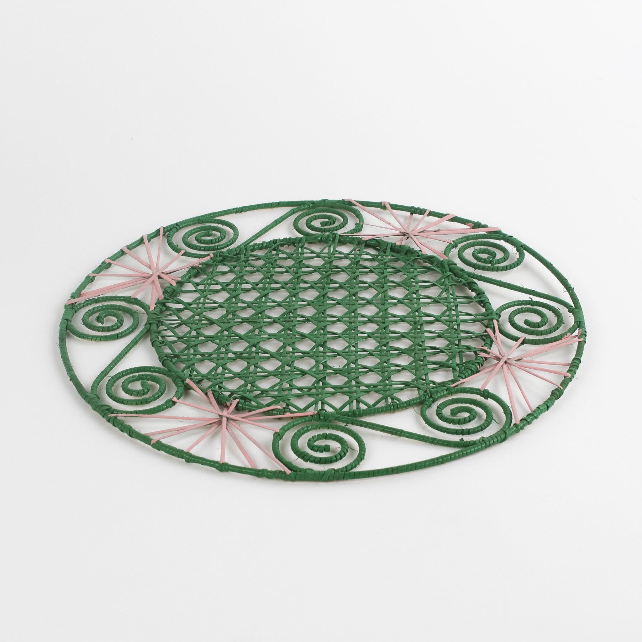 a pink and green round rattan placemat with green swirls and pink star woven motifs against a white backround.