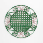 a pink and green round rattan placemat with green swirls and pink star woven motifs against a white backround.