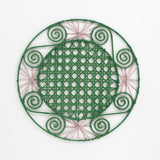 a pink and green round rattan placemat with green swirls and pink star woven motifs against a white backround.