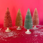 A set of 4, Pastel Bottle Brush Christmas Trees in shades of pink and one green against a red, snow covered background. 