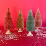 A set of 4, Pastel Bottle Brush Christmas Trees in shades of pink and one green against a red, snow covered background. 