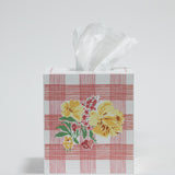 a pink gingham tissue box cover with a central yellow floral motif on the front. 