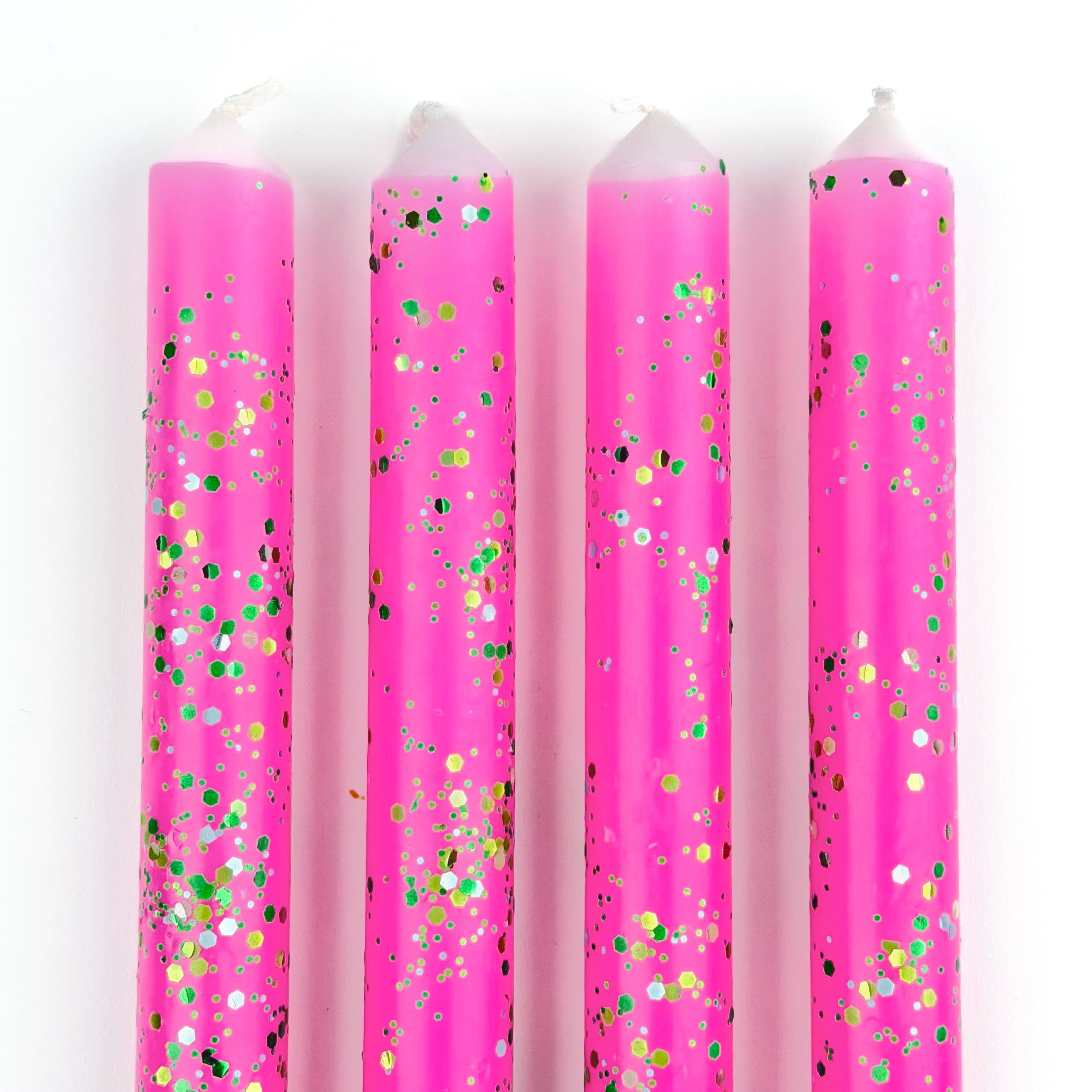 Pink glitter taper candles with green and gold confetti-style sparkle detailing for festive table decor.