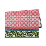A pink and green chinoiserie tea towel featuring a central pink lattice pattern and green floral border against a white background. 