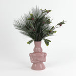 Pink nutcracker vase filled with greenery on a white background