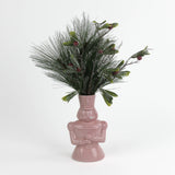 Pink nutcracker vase filled with greenery on a white background