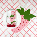 strawberry paper placemat spring table setting with white plate and strawberry napkin on red lattice tablecloth.