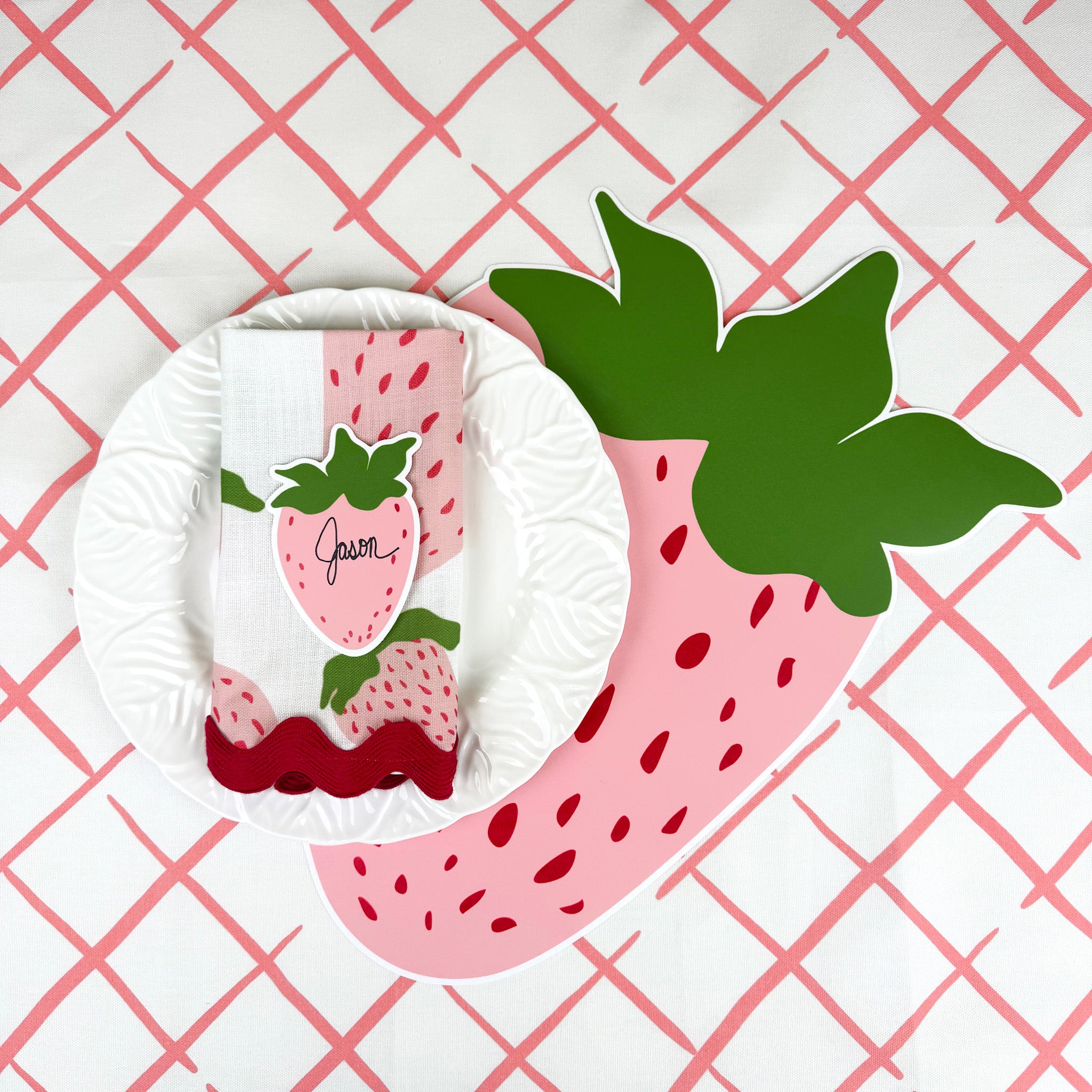 strawberry paper placemat spring table setting with white plate and strawberry napkin on red lattice tablecloth.