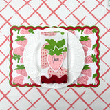 strawberry paper placemat spring table setting with white plate and strawberry napkin on patterned tablecloth.