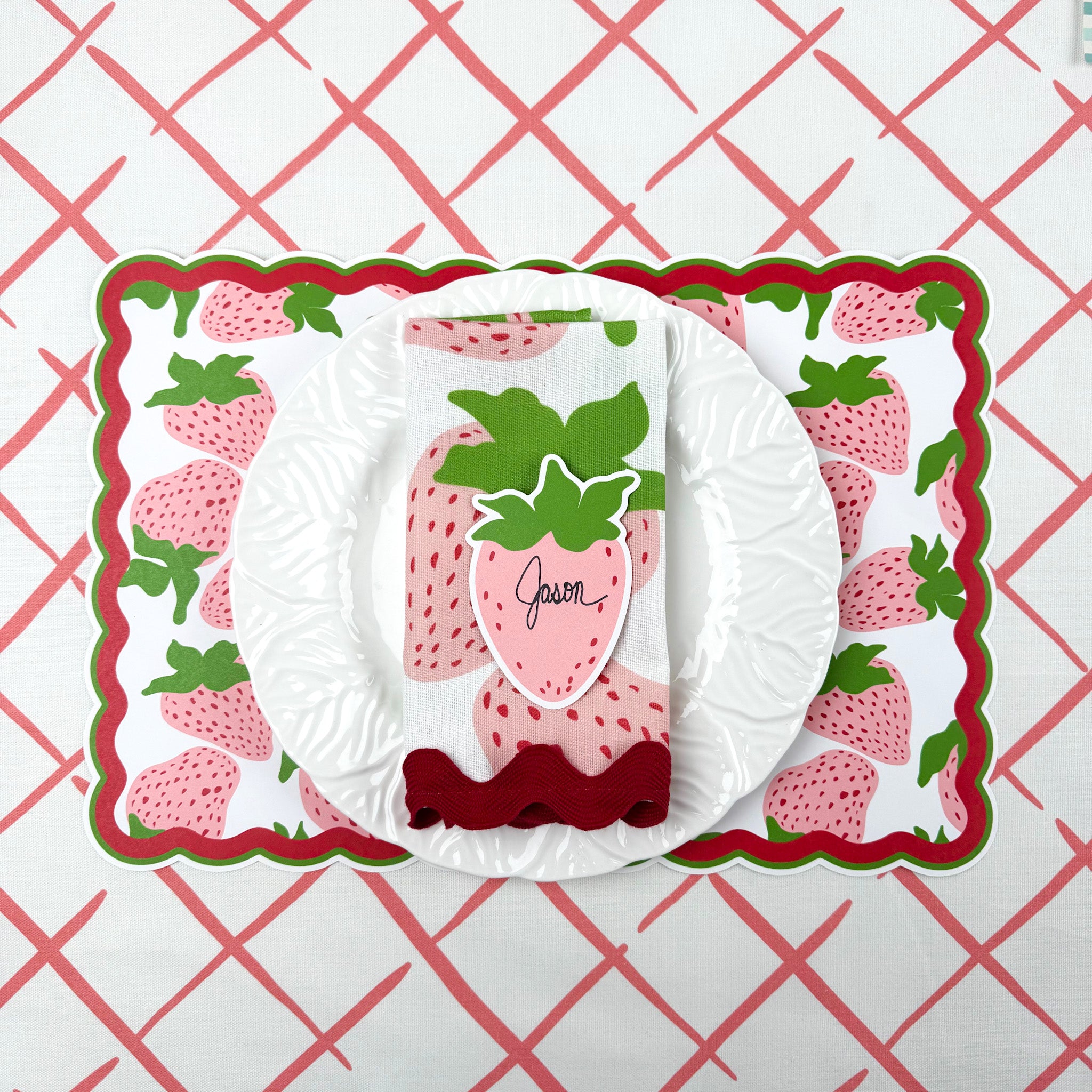 strawberry paper placemat spring table setting with white plate and strawberry napkin on patterned tablecloth.