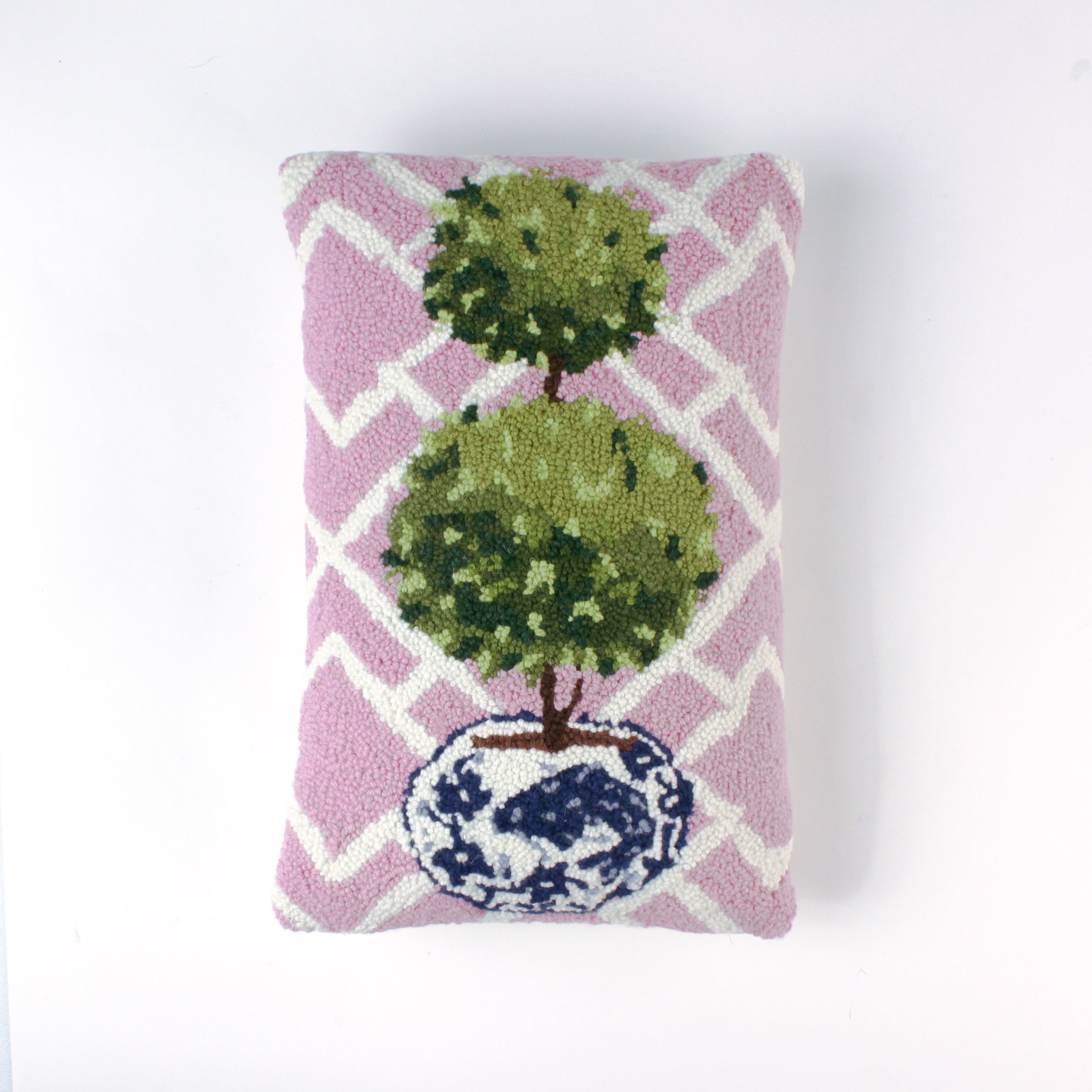 Rectangular decorative pillow with a pink and white lattice background featuring a green double topiary plant in a blue and white chinoiserie-style pot.