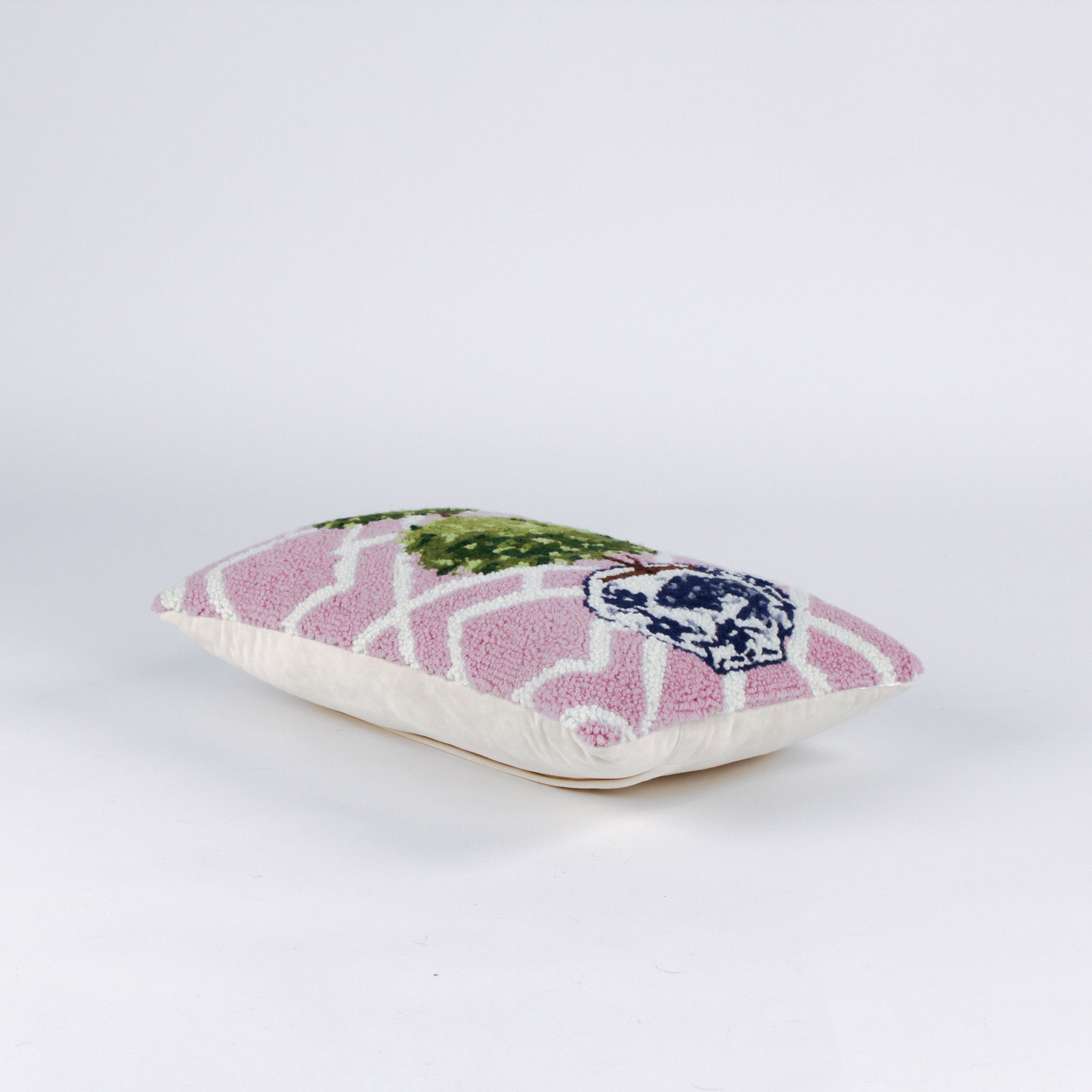 side of a Rectangular decorative pillow with a pink and white lattice background featuring a green double topiary plant in a blue and white chinoiserie-style pot.