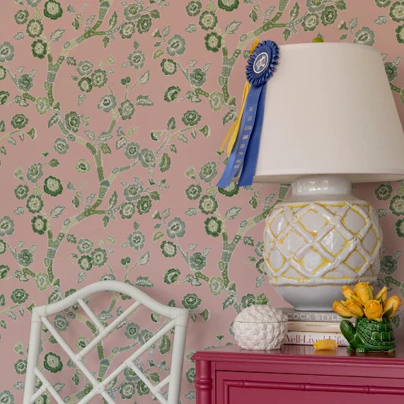 a white chair and lamp against a wall of pink and green chinoiserie wallpaper