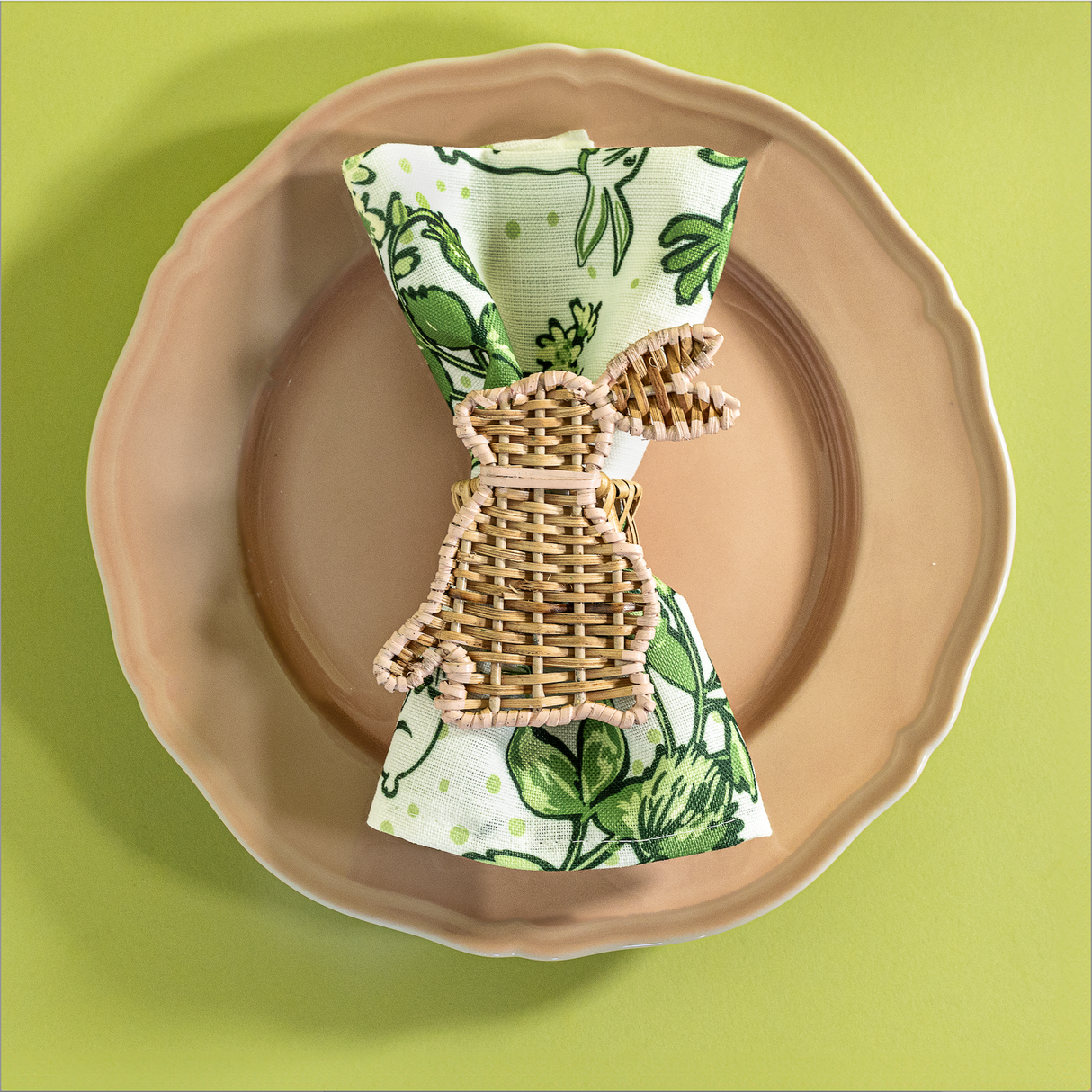A green bunny and strawberry print fabric Easter napkin resting on a pink plate