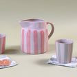 pink and white striped ceramic pitcher with ceramic cups and gingham cocktail napkins