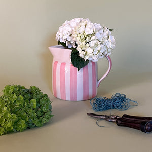 pink and white striped pitcher with flowers in it.