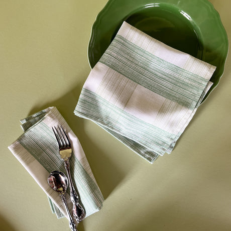 two green gingham dinner napkins in gin lane print fabric by madap cottage resting on a green plate on a light green background