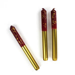 3 plum pudding gold taper candles lying in a white background