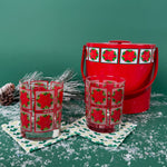 2 poinsettia-printed Christmas glasses with a matching red holiday ice bucket on a snowy green background