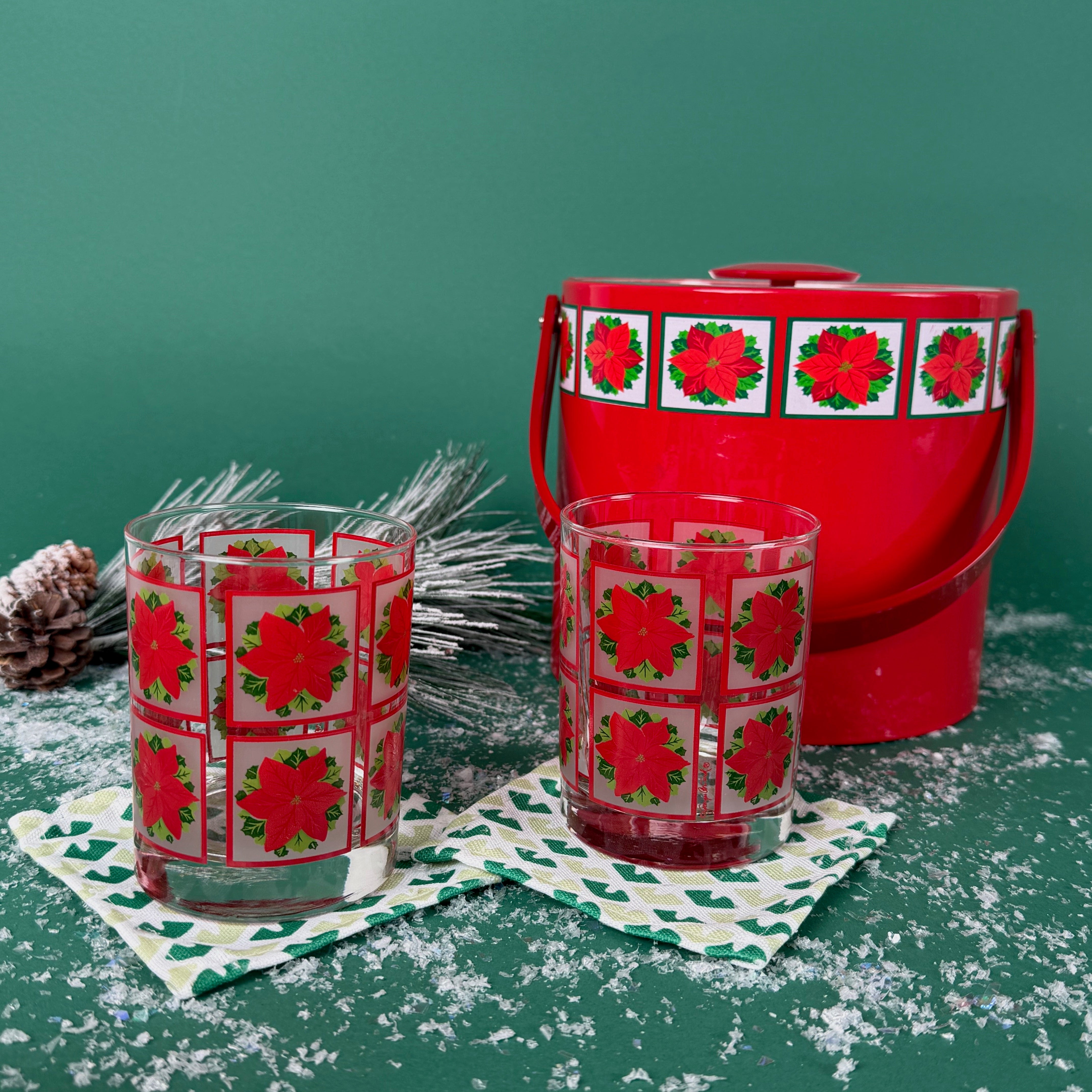 2 poinsettia-printed Christmas glasses with a matching red holiday ice bucket on a snowy green background