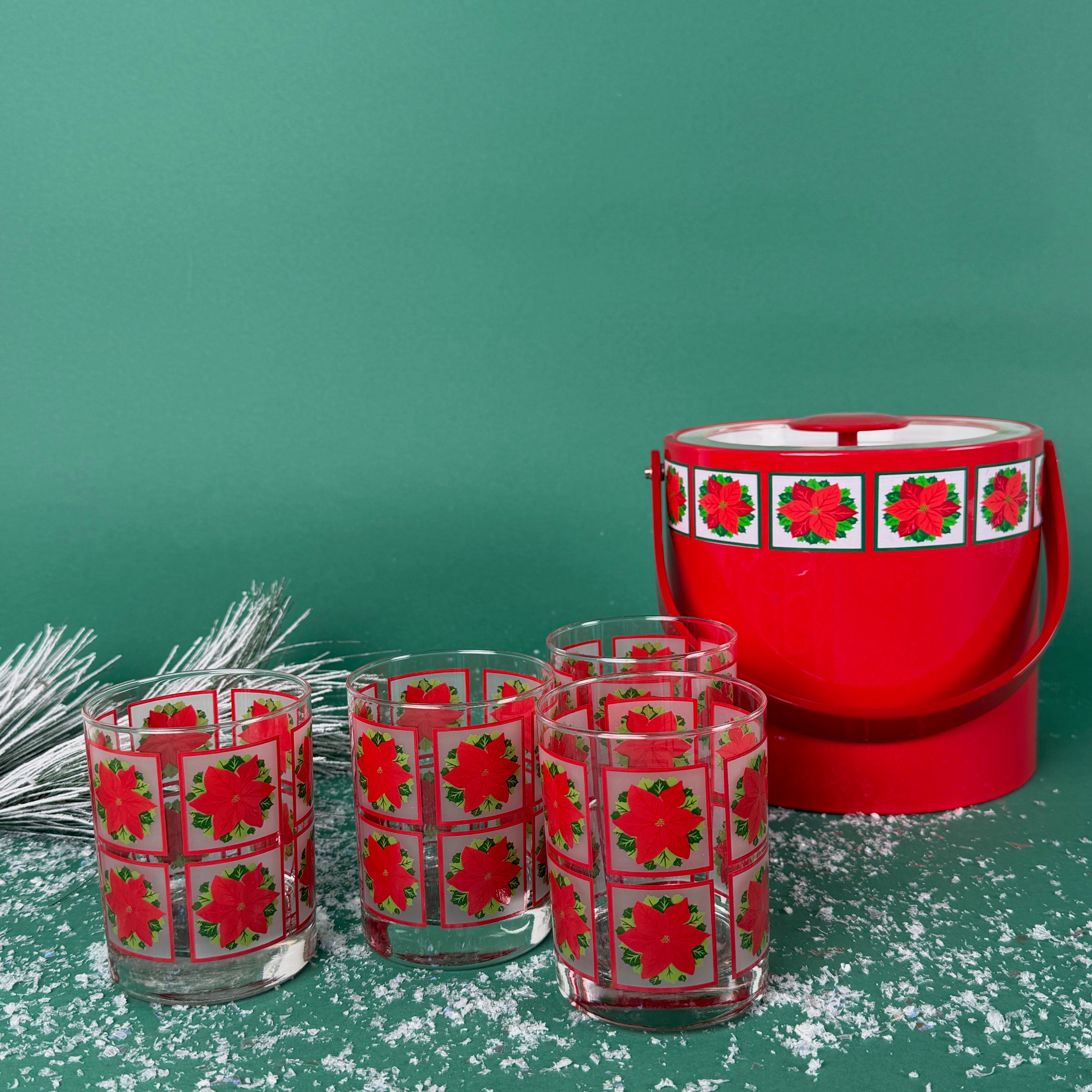 Set of poinsettia-printed Christmas glasses with a matching red holiday ice bucket on a snowy green background