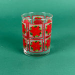Clear drinking glass decorated with red poinsettia squares on a green background