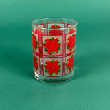 Clear drinking glass decorated with red poinsettia squares on a green background
