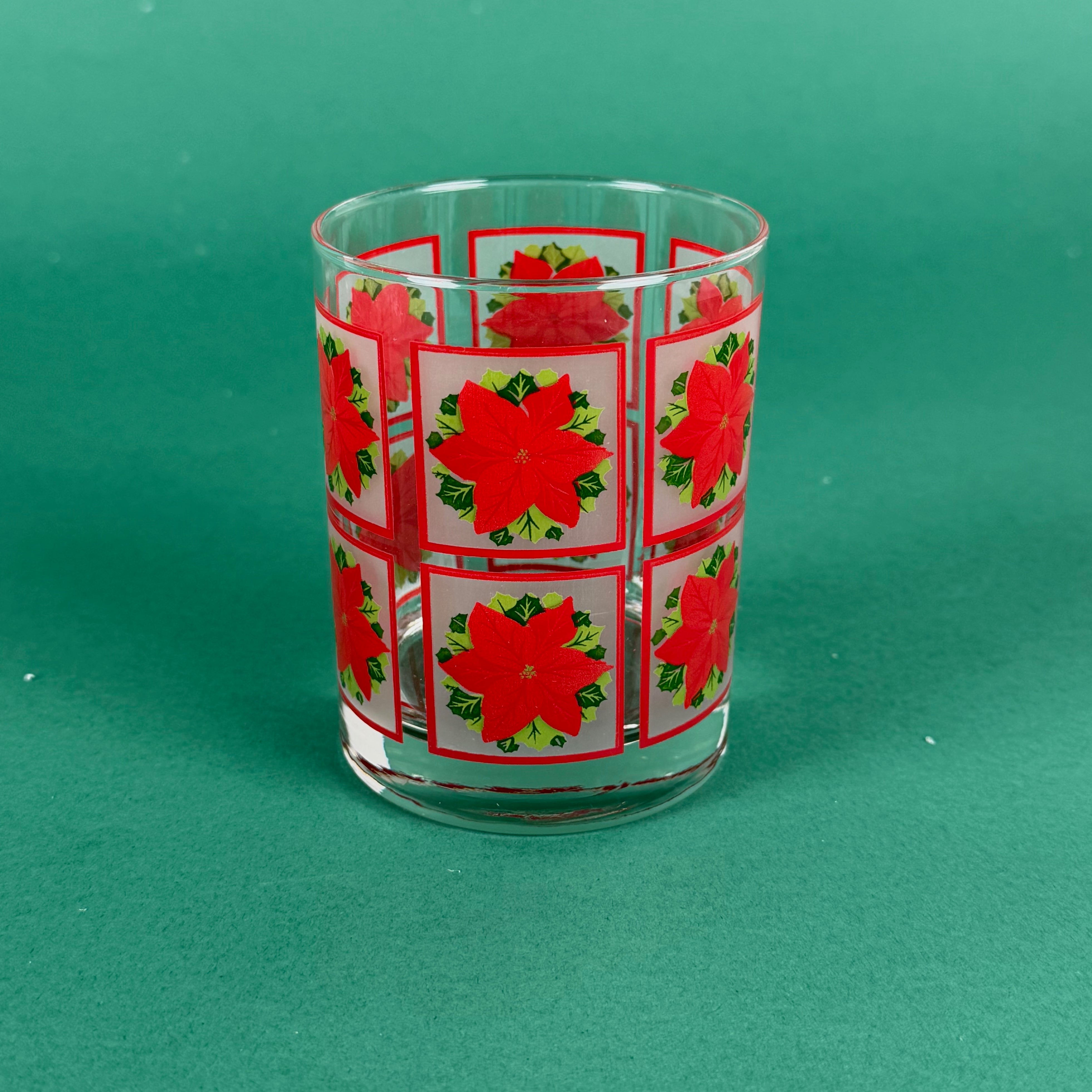 Clear drinking glass decorated with red poinsettia squares on a green background