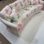 A curved, vintage floral sofa featuring pink flowers on a white background. 